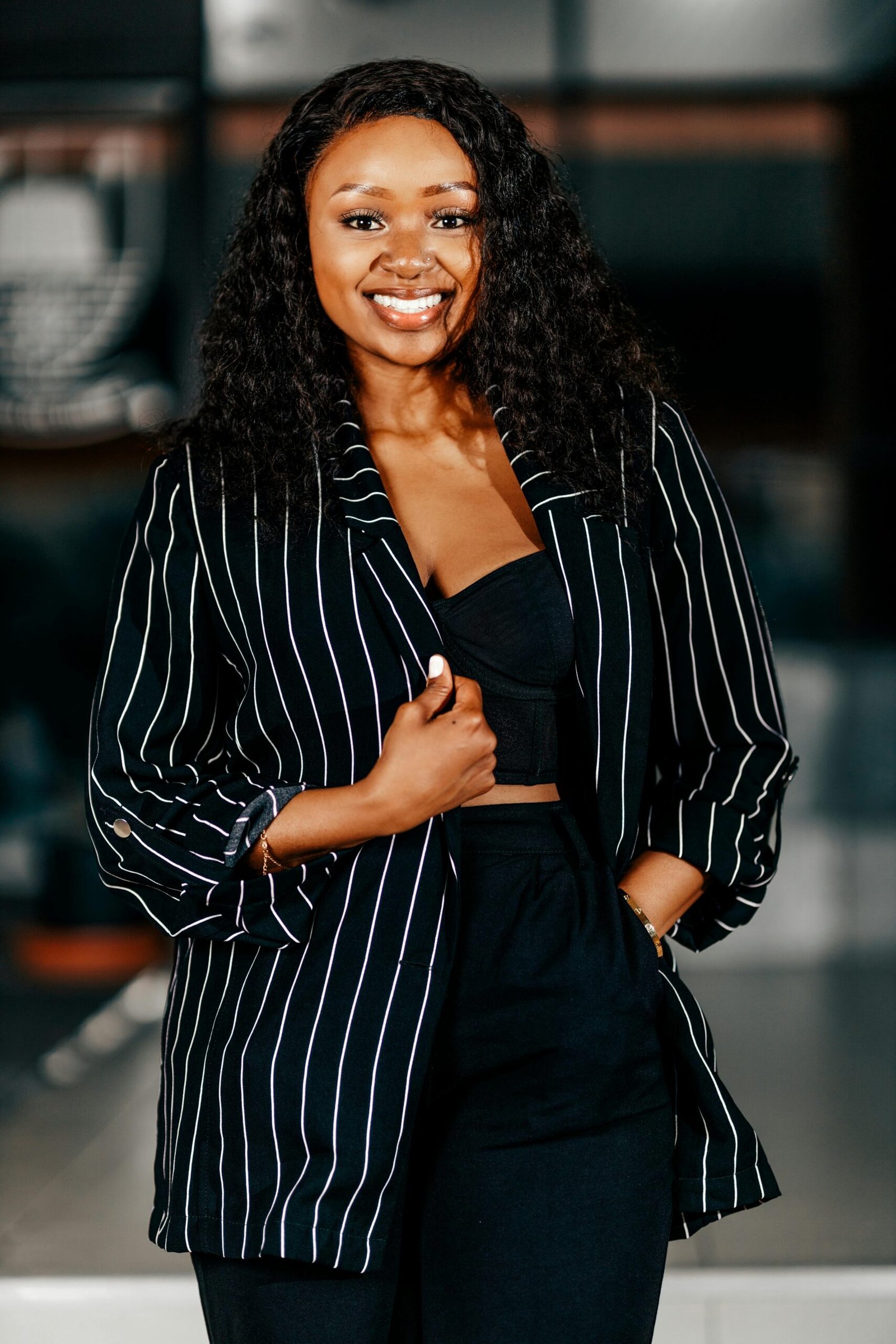 Stylish woman in a black striped blazer smiling confidently indoors.
